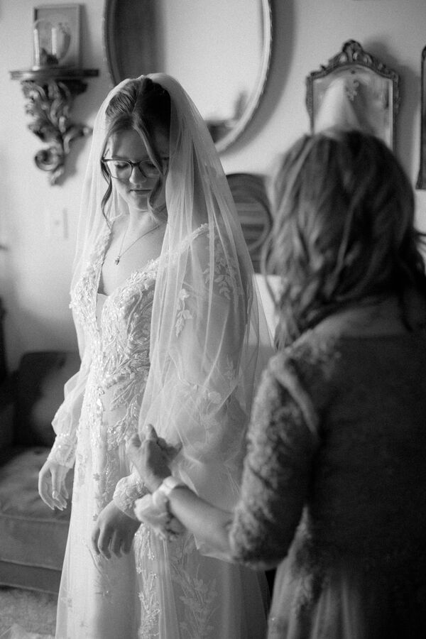 Black and white bride in a lace gown and veil while her mother helps with a bracelet