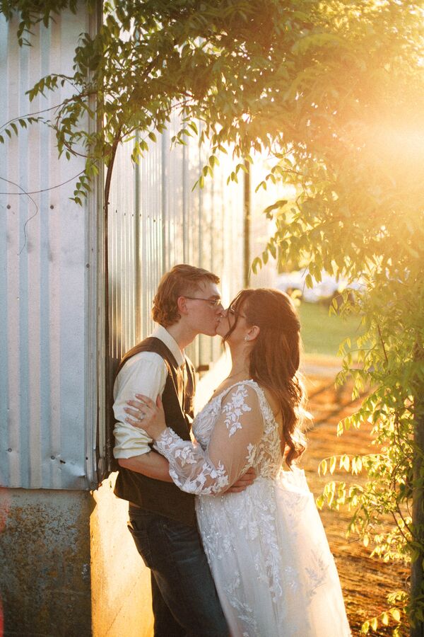 Couple kissing in golden-hour light against a metal barn wall